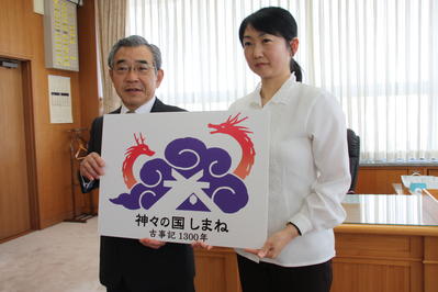松谷さんと最優秀ロゴマークを挟んで記念撮影する知事の写真